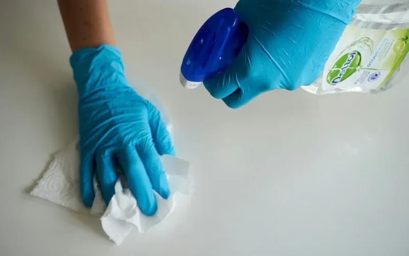 Gloved hands disinfecting a countertop with spray and a cloth