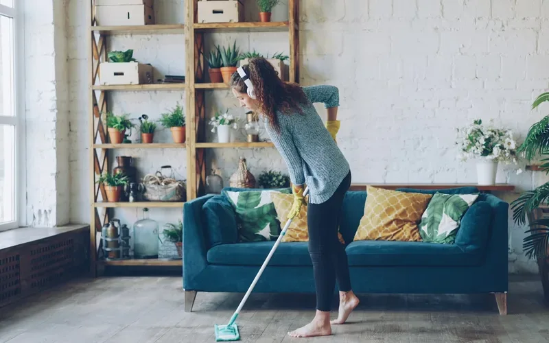 Person mopping the floor of a tidy, plant-filled living room