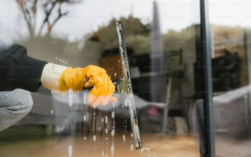 Gloved hand pulling a squeegee down a large window pane
